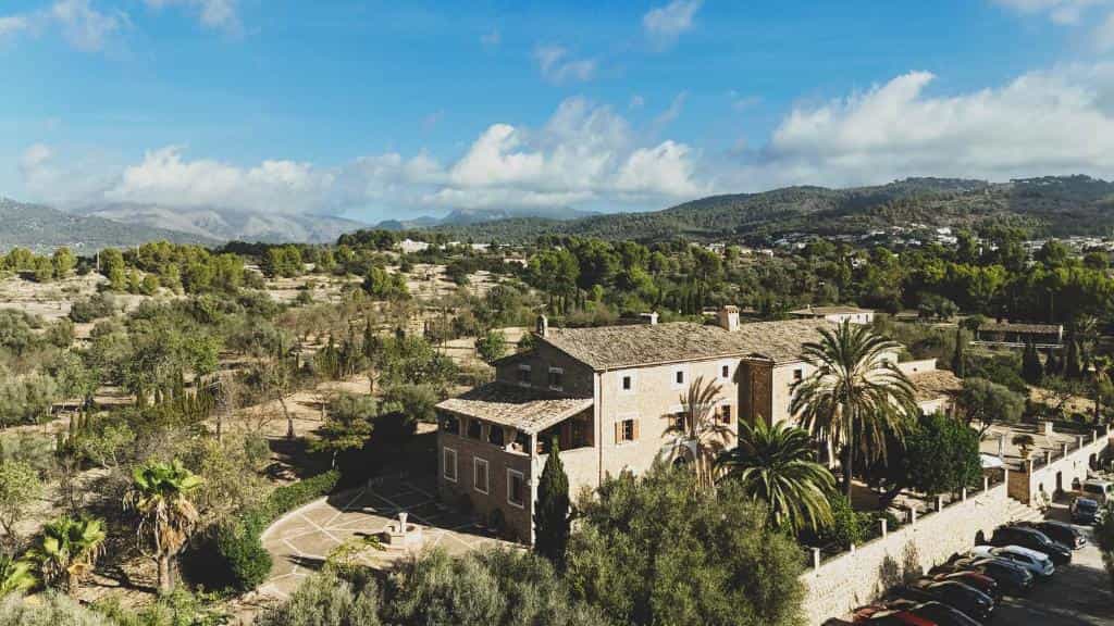 Stone finca with palm trees surrounded by green hills under a blue, cloudy sky, Finca Can Estades