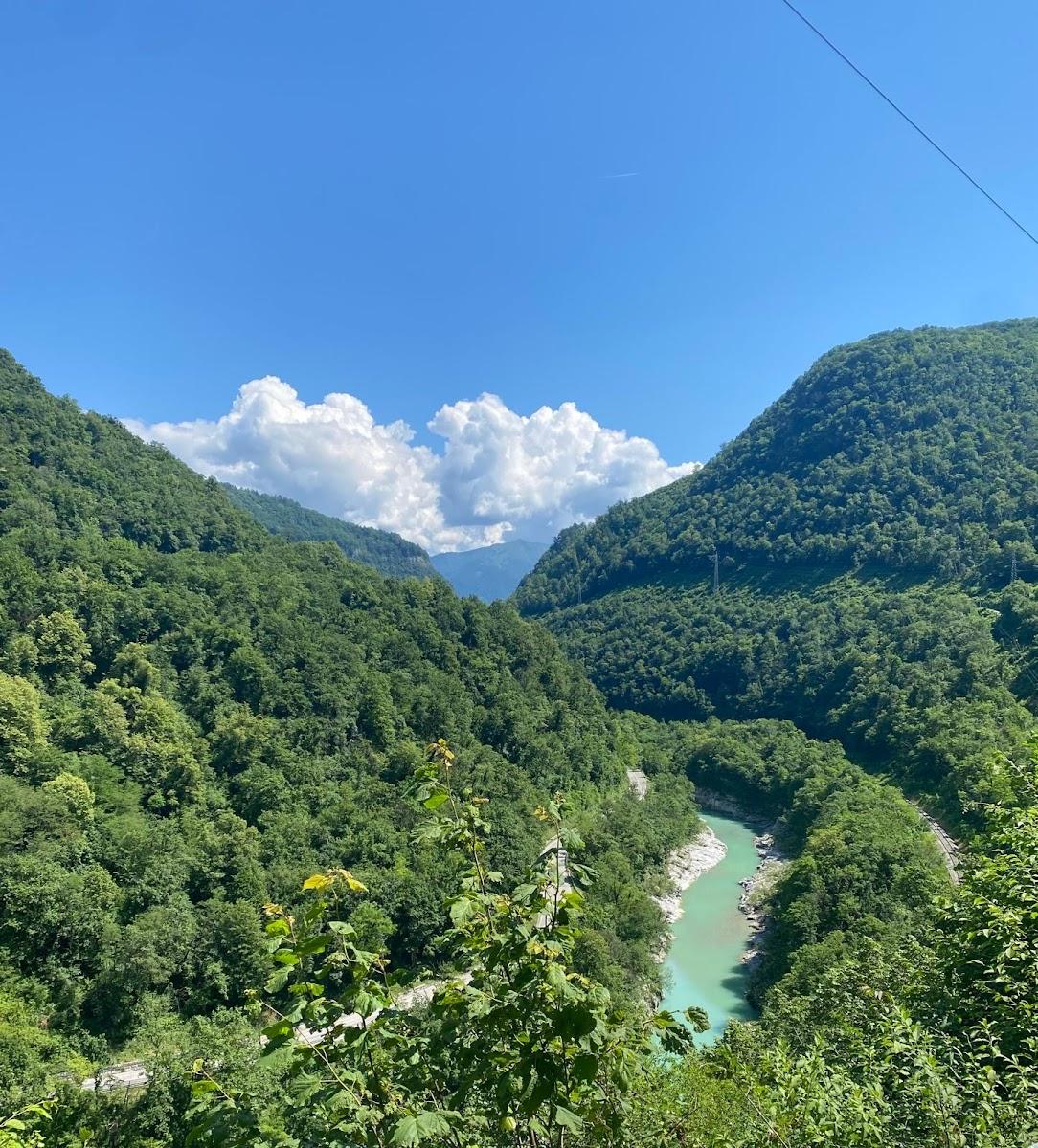 Turquoise river winding through steep, densely forested mountains under a blue sky with white clouds.