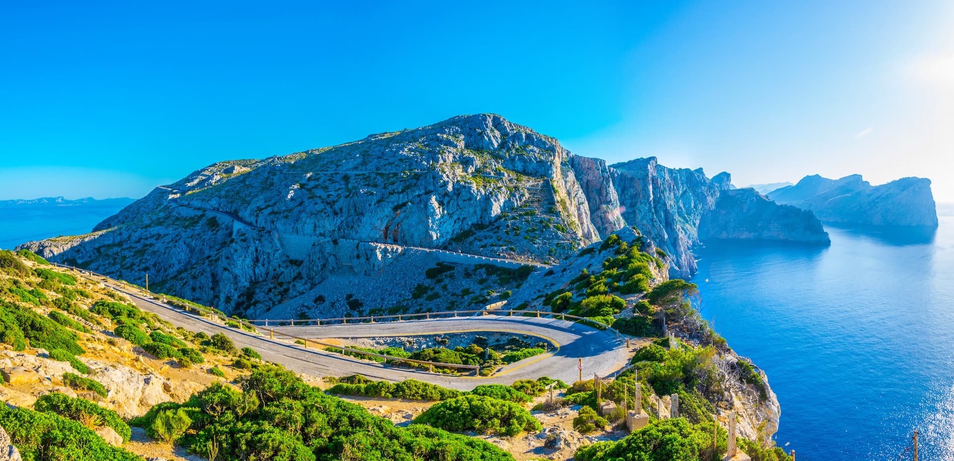 Winding mountain road above steep cliffs overlooking the bright blue sea in Mallorca, Spain.