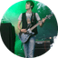 Musician playing electric guitar on stage with green lighting and amplifier equipment