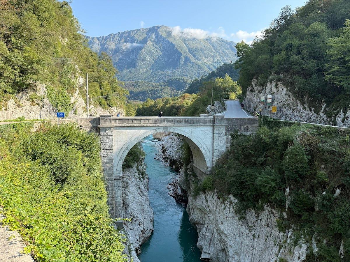Stone arch bridge over turquoise river canyon with lush green mountains in background