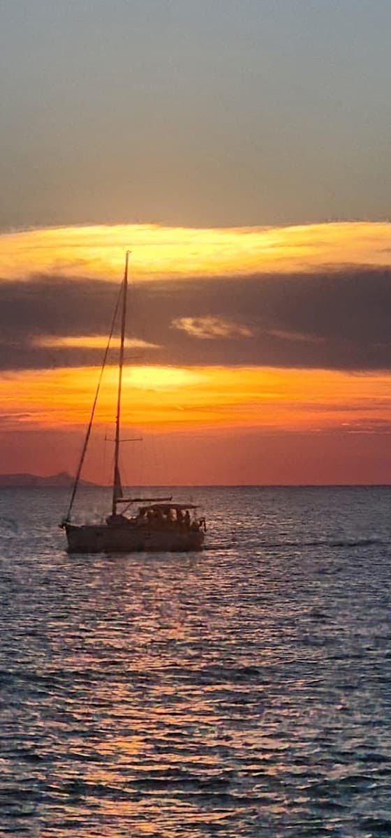 Sailboat on the water during a vibrant orange and yellow sunset over the sea.