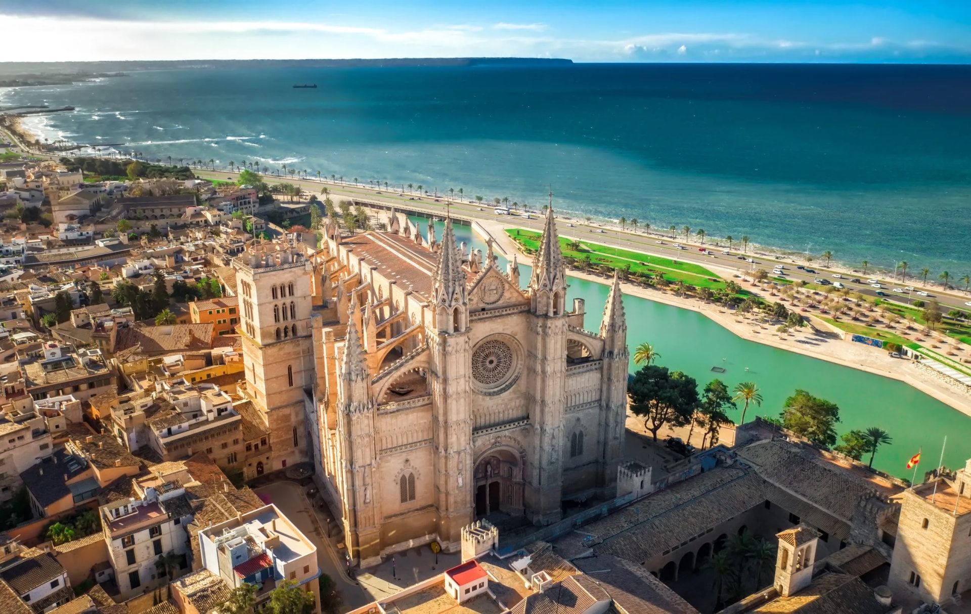 Aerial view of Palma Cathedral next to turquoise water and the Mediterranean Sea.