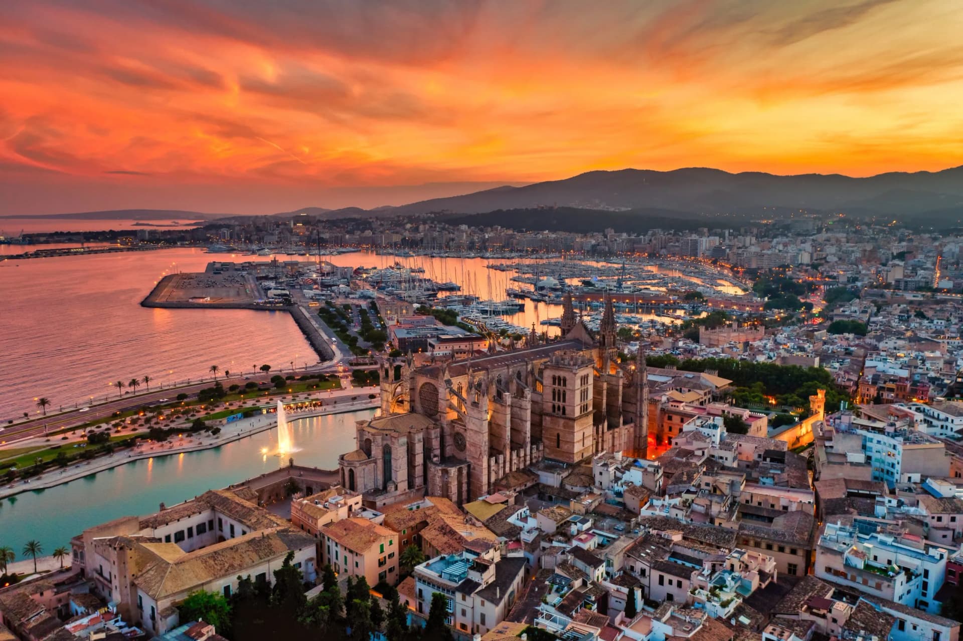 La Seu Cathedral at sunset over Palma de Mallorca city, harbor, and mountains.